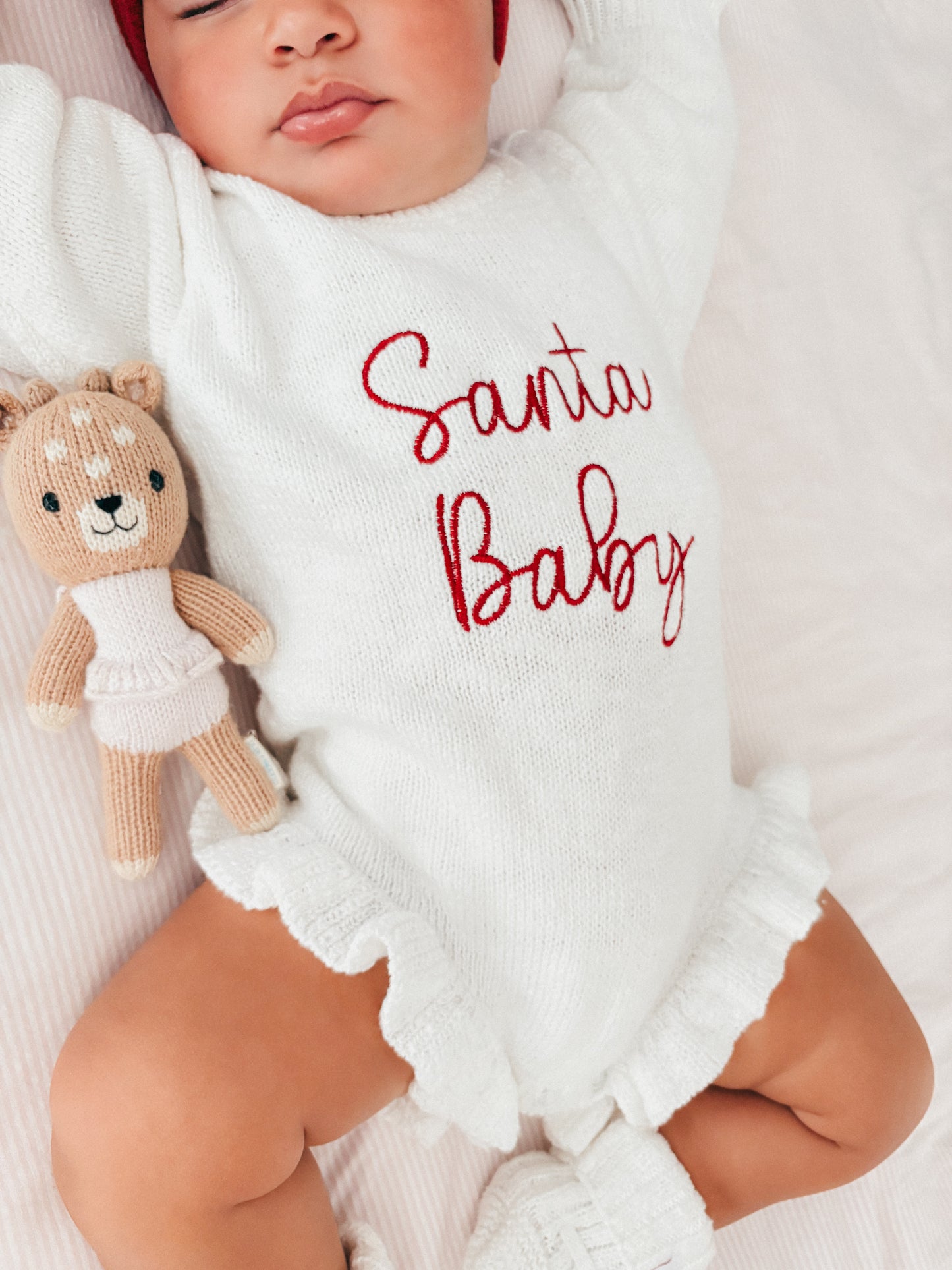 Baby wearing a white romper with 'Santa Baby' embroidery
