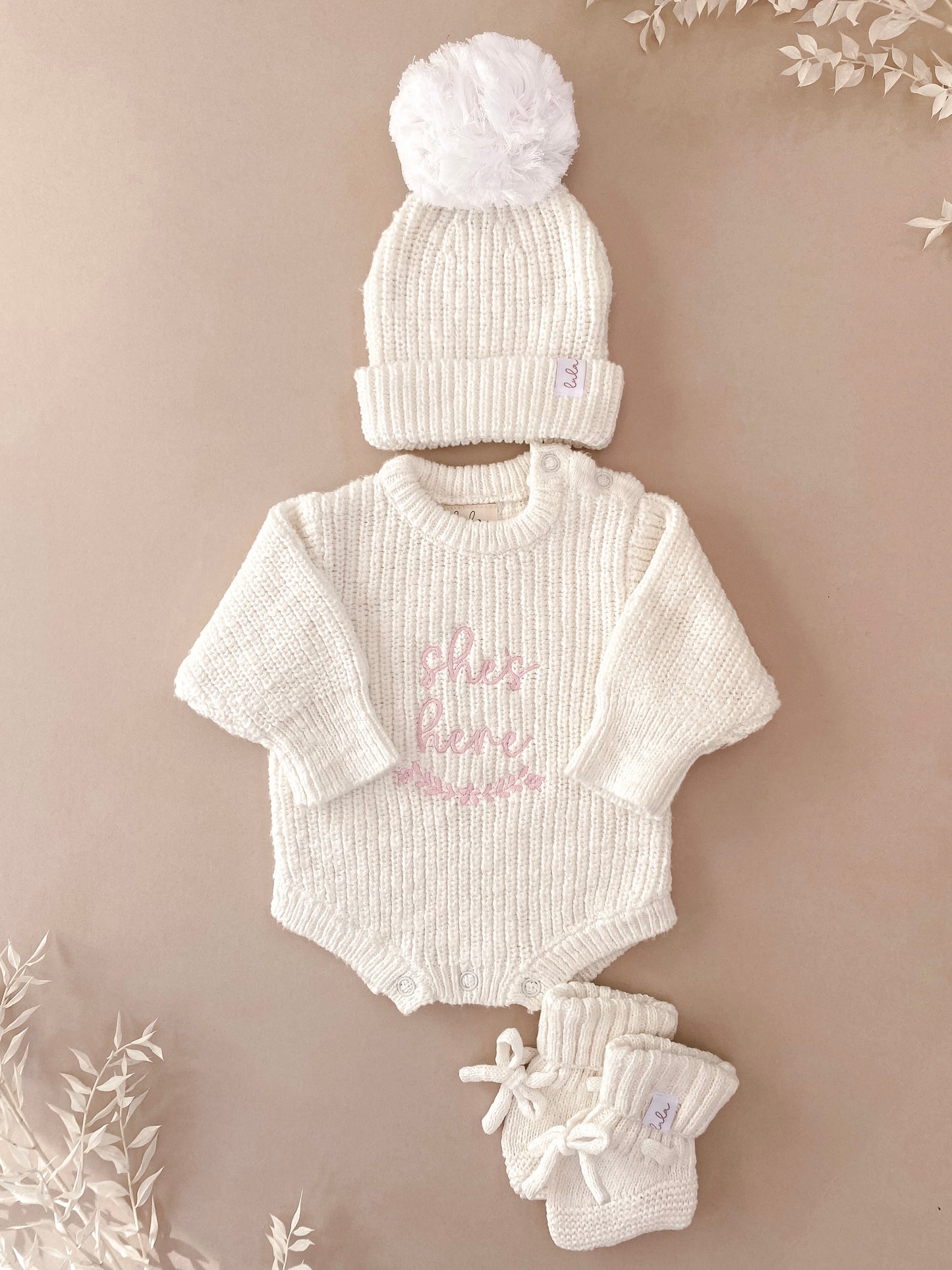 knitted ivory baby outfit set with hat, 'she's here' romper, and booties.