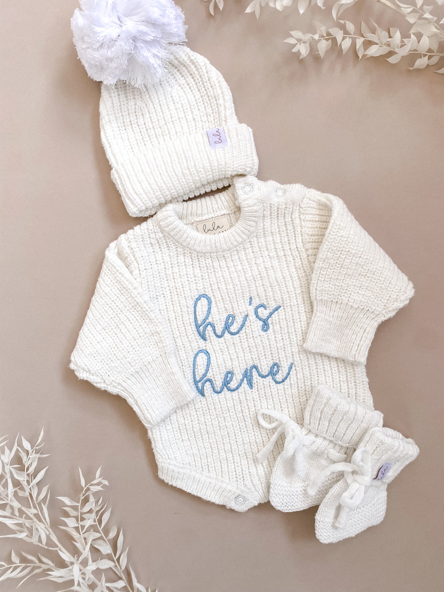 Baby outfit set with white romper, hat, and booties on a beige background