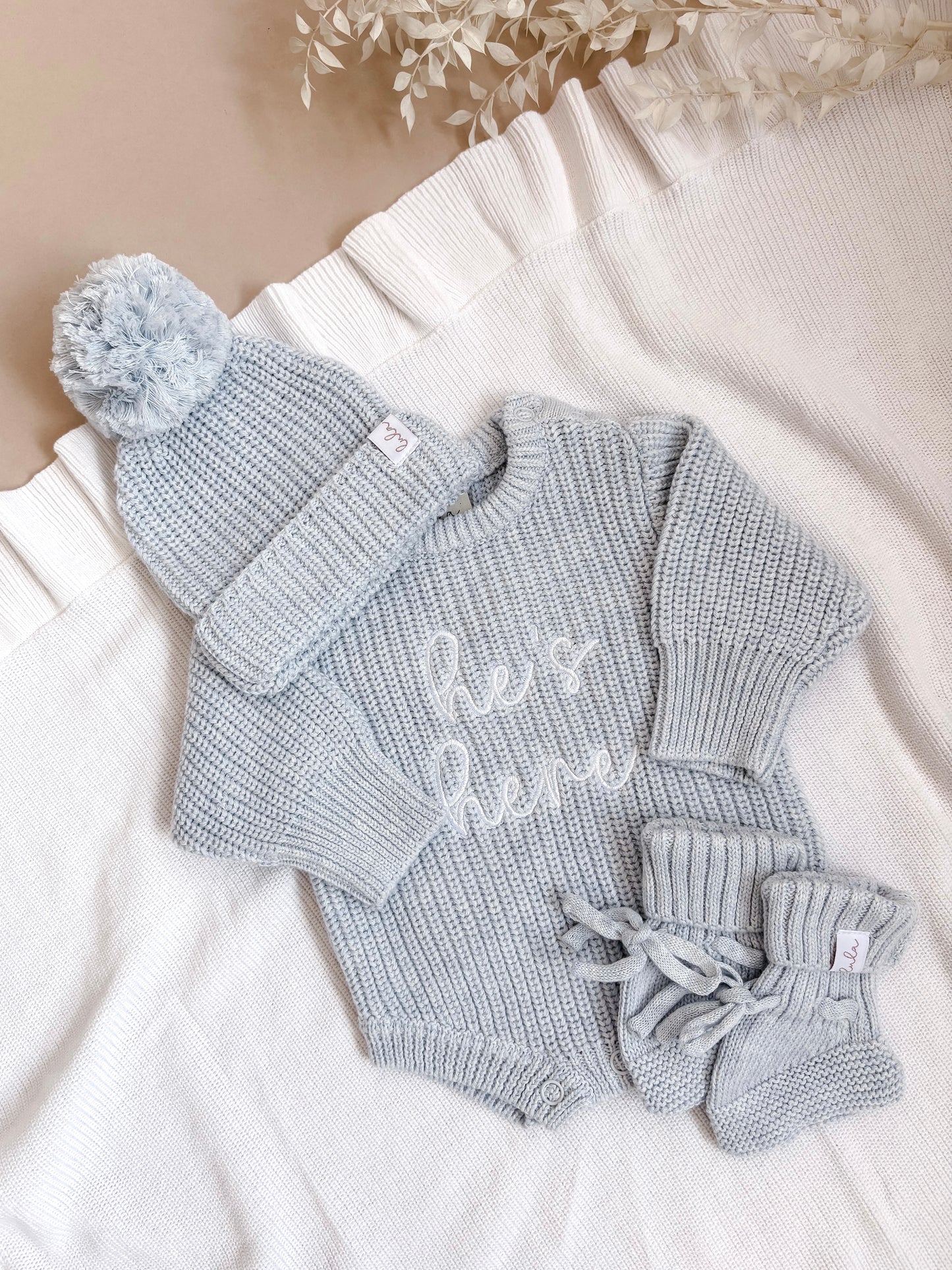 Baby blue newborn knitted outfit set with 'he's here' romper, hat, and booties.