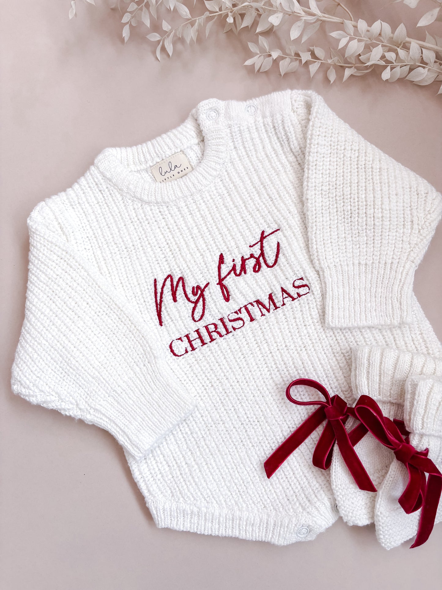 White baby romper with 'My first Christmas' text and matching booties on a beige background