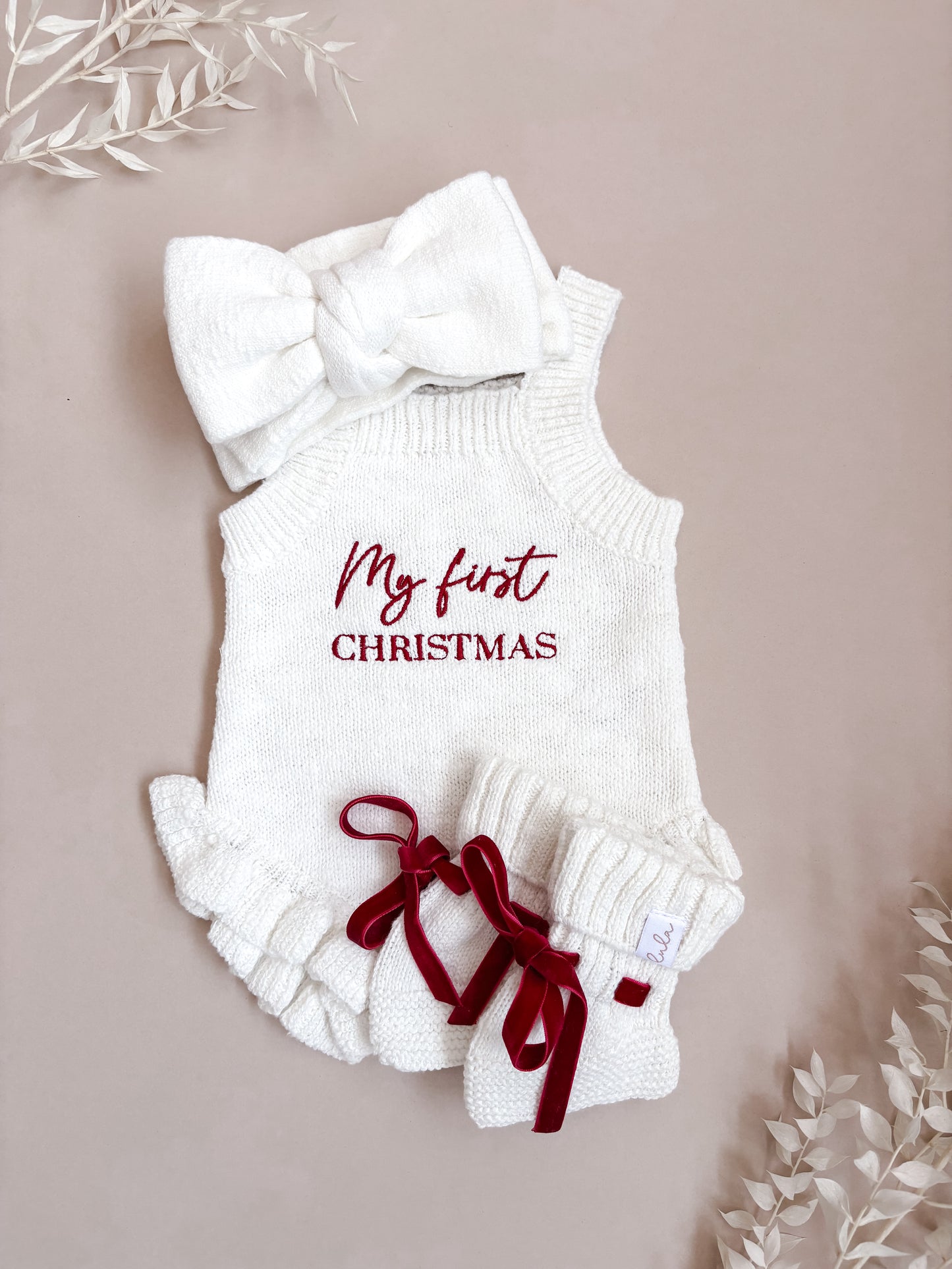 White baby romper with red text and bow on a beige background