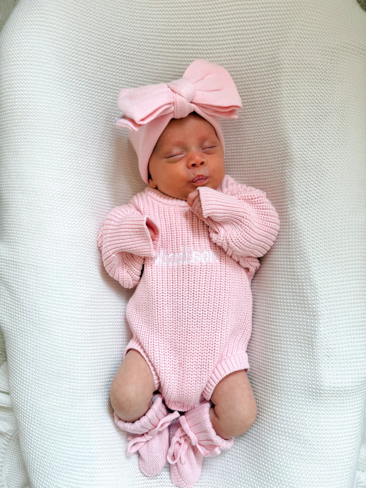 Newborn baby girl in a pink knitted romper with a matching bow on a white blanket