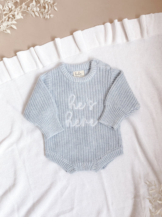 Light blue baby romper with 'He's here' embroidery in white thread