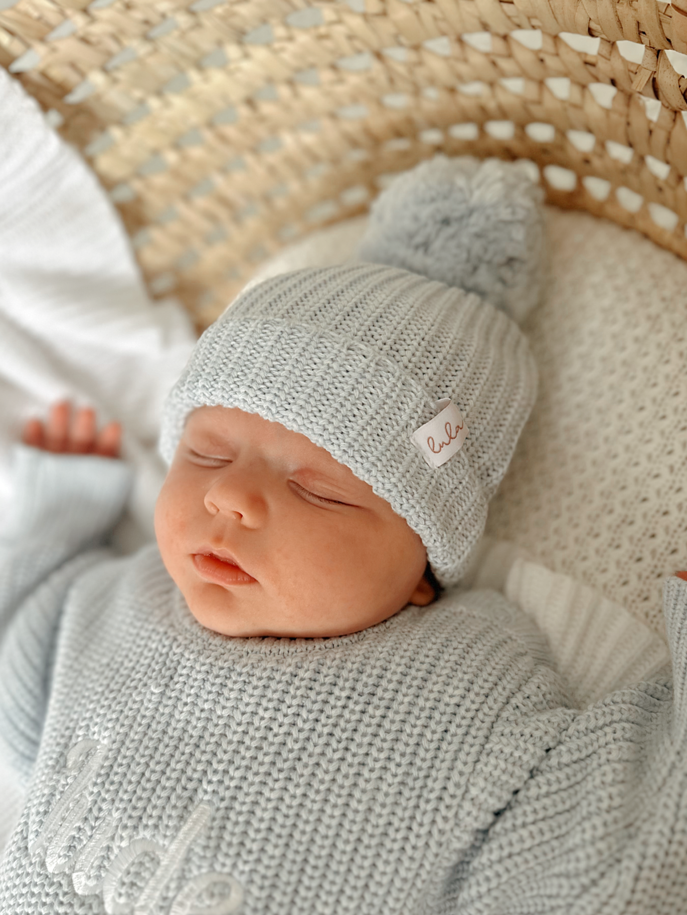 Newborn baby sleeping in a basket wearing a blue knit romper with a matching hat.