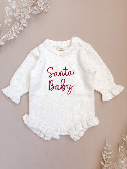 White baby romper with 'Santa Baby' text on a beige background