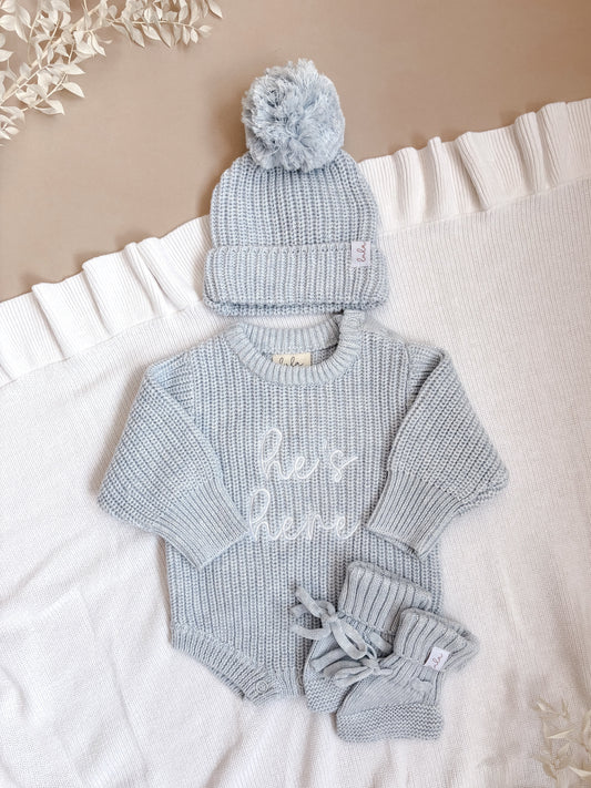 Baby blue newborn outfit set with 'he's here' romper, hat, and booties.