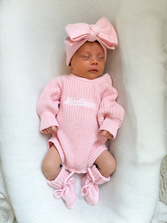Newborn baby in a pink knitted romper with a matching topknot bow and booties