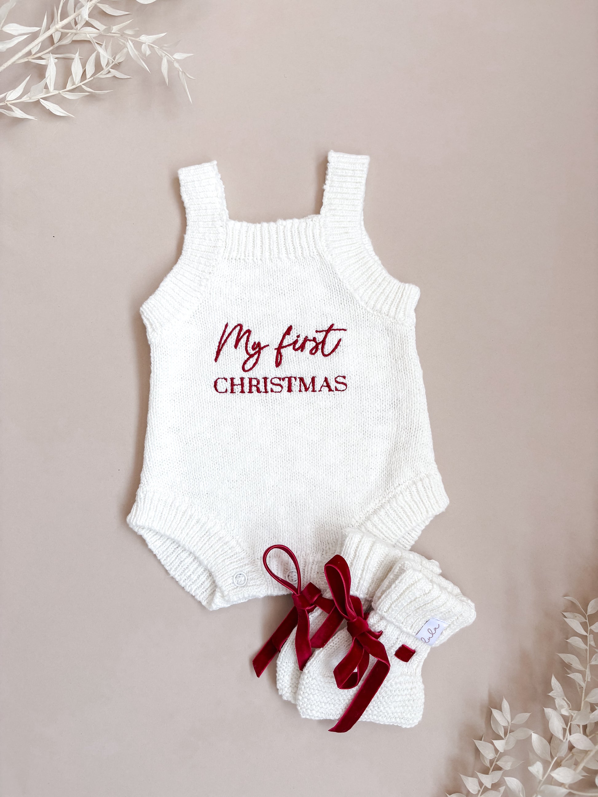White baby romper with 'My first Christmas' embroidery on a beige background