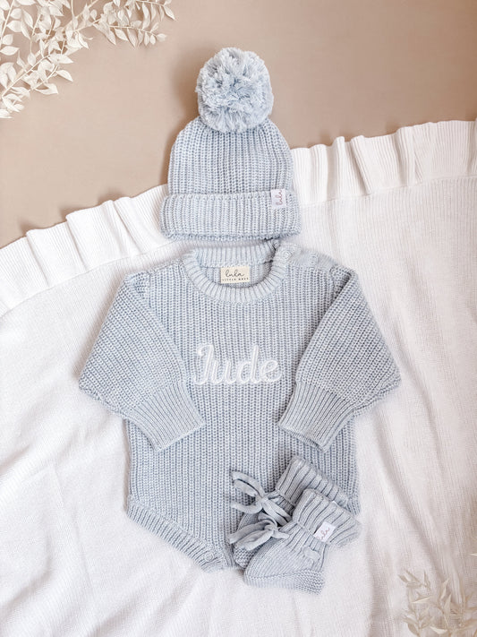 blue baby outfit with matching hat and booties on a white blanket.